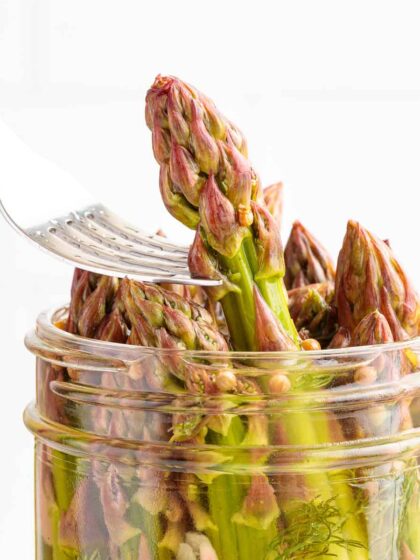 A fork lifts a stalk of pickled asparagus out of a jar of Quick Pickled Asparagus