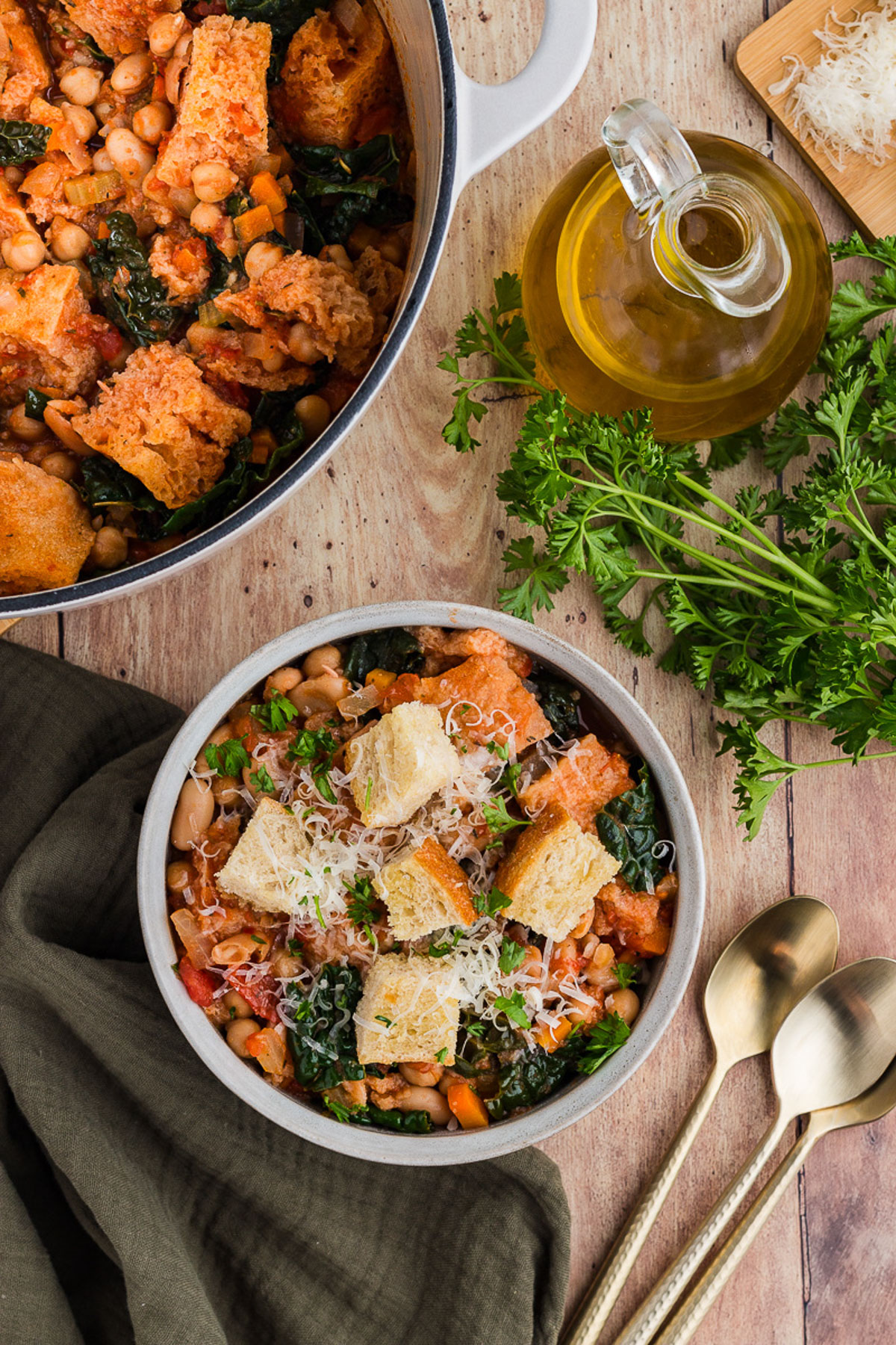 Ribollita in a pot and in a bowl ready to serve with a bottle of olive oil and parsley in the background.