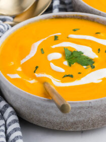 Roasted carrot soup in a rustic bowl with coconut milk and parsley on top. A striped napkin is alongside.