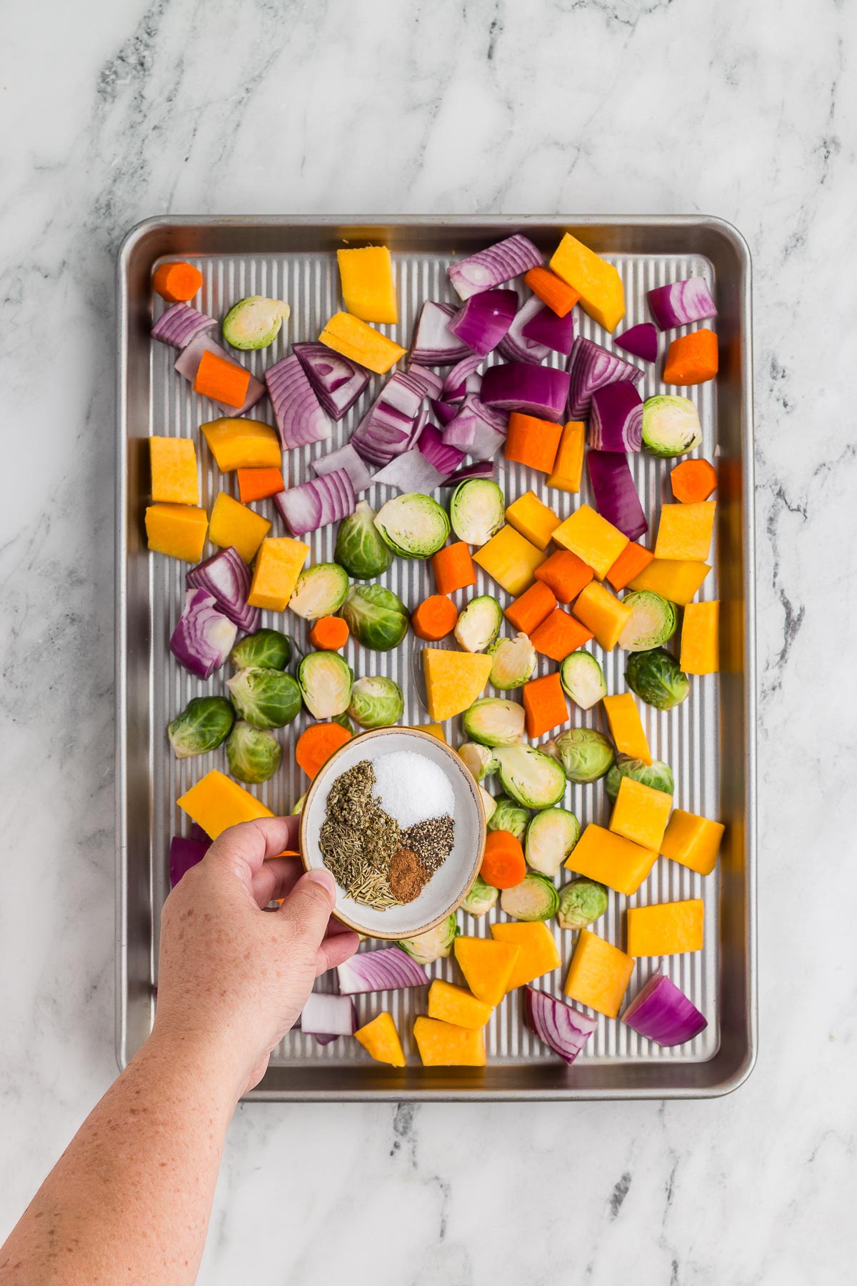 Adding seasonings to Roasted Fall Vegetables on a baking sheet
