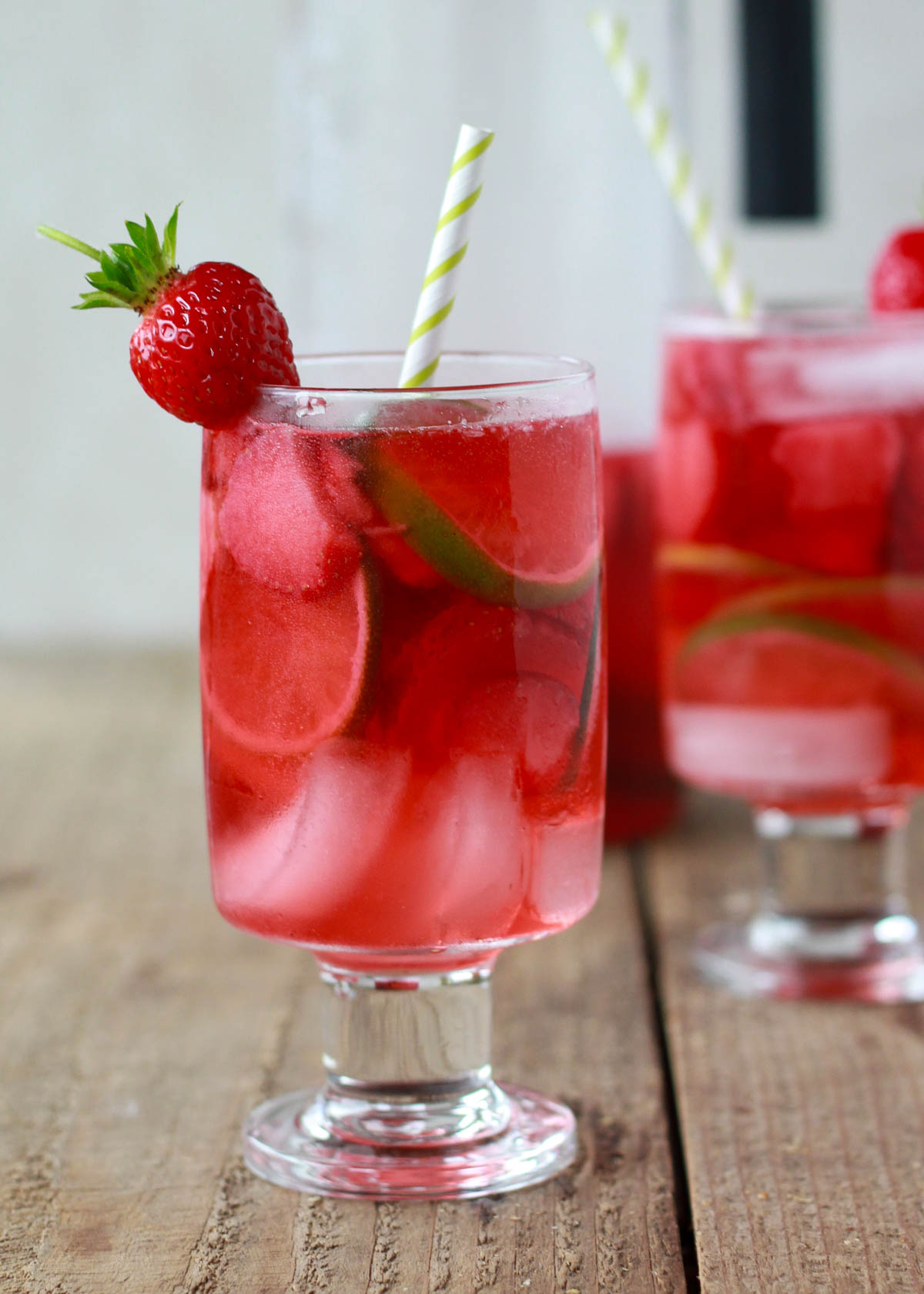 Two glasses of rose sangria in clear glass with straws and a strawberry garnish