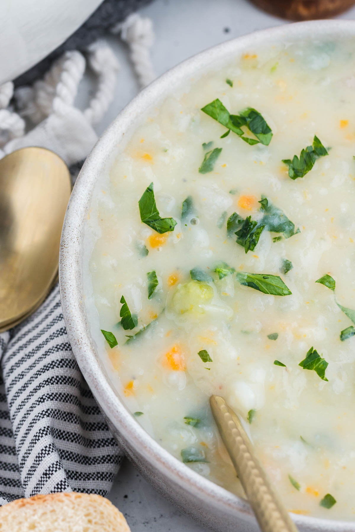 Potato soup with parsley for garnish in a white bowl. A gold spoon is perched inside.