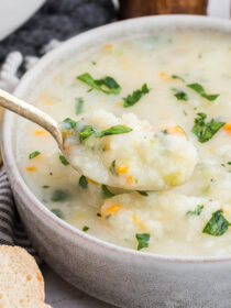 A spoonful of potato soup is scooped out of a white bowl.