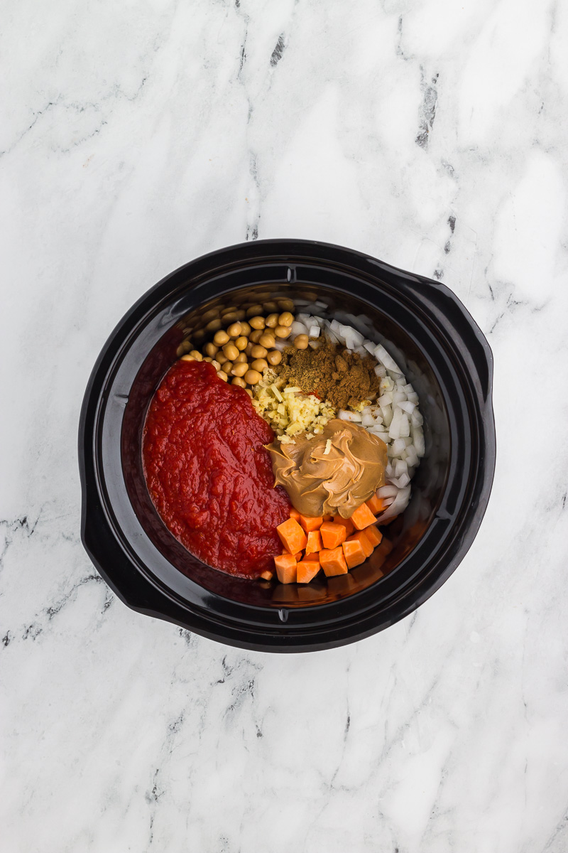 Top view of ingredients for Slow Cooker Sweet Potato, Chickpea, & Peanut Stew in a Crock Pot, ready to cook.
