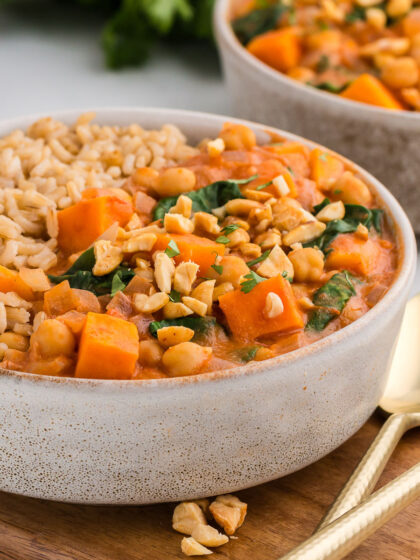 Slow Cooker Sweet Potato, Chickpea, & Peanut Stew in a white pottery bowl with gold spoons.