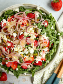 A top view of strawberry arugula salad with wooden salad tossers.