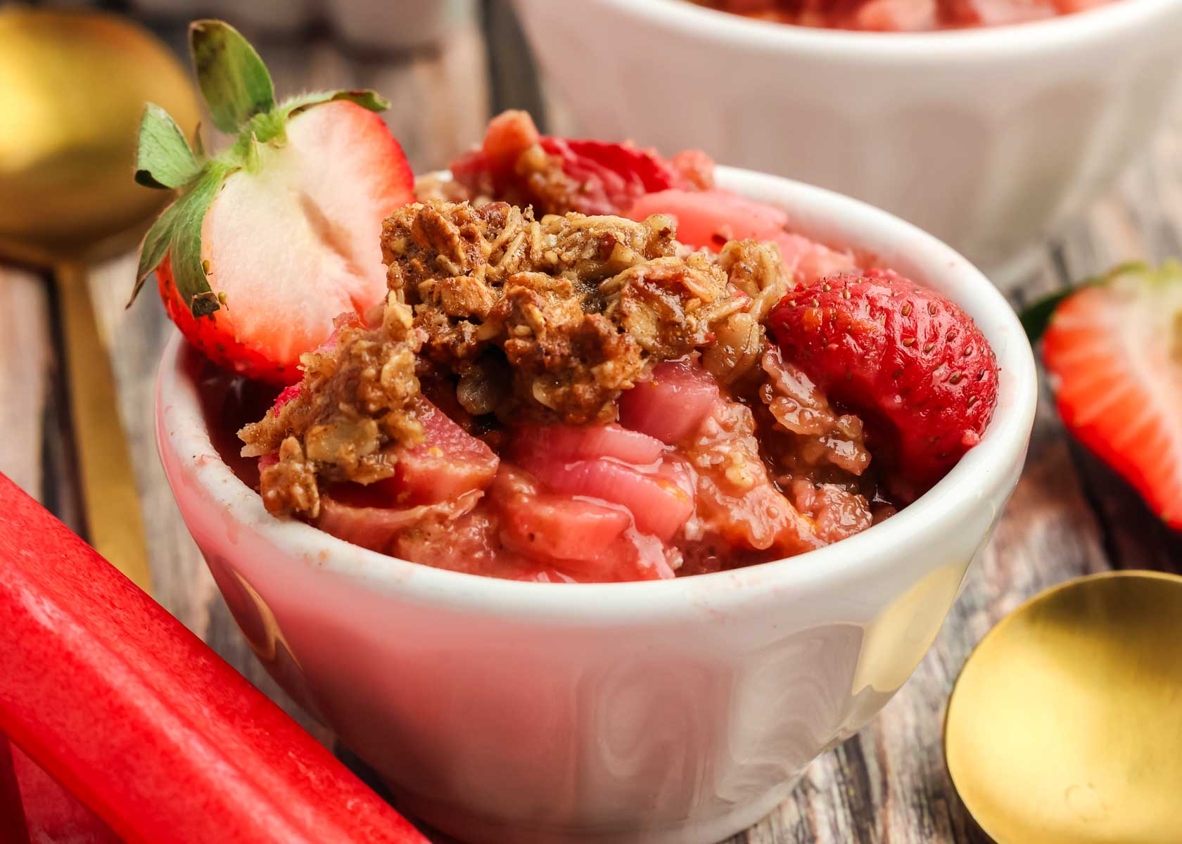 white bowl full of Strawberry Rhubarb Crisp with rhubarb in the foreground