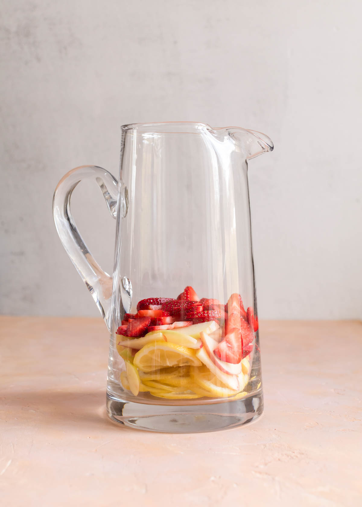 Fruit in a clear glass pitcher, ready to make sangria.