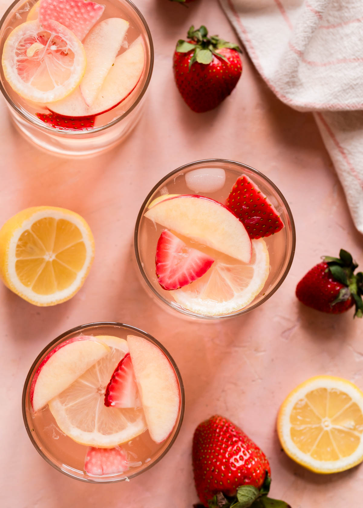A top view of two glasses of sangria on a pink background with strawberries and lemons.