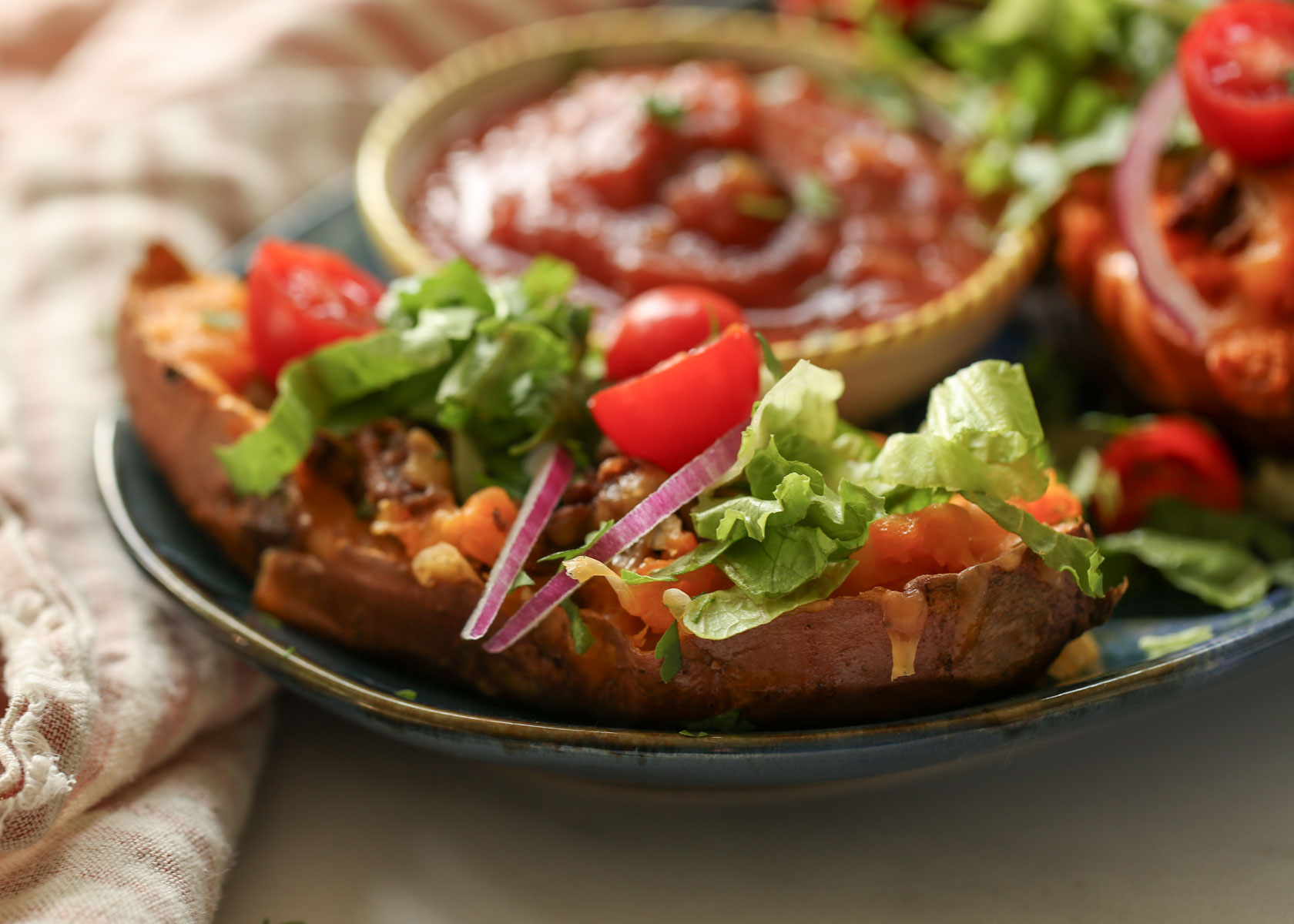 Side-view of a taco stuffed sweet potato with lettuce and cherry tomatoes.