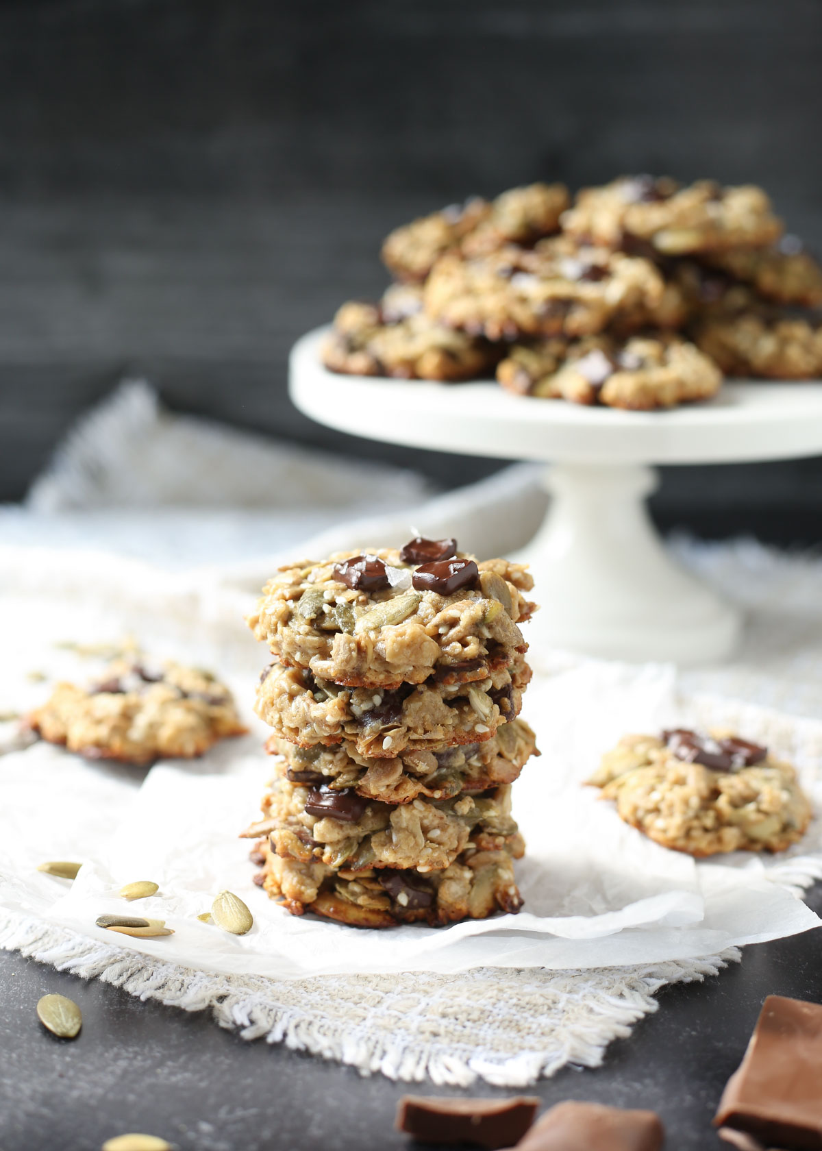 A stack of tahini seed cookies on a piece of parchment paper and more healthy chocolate chip cookies in the background.