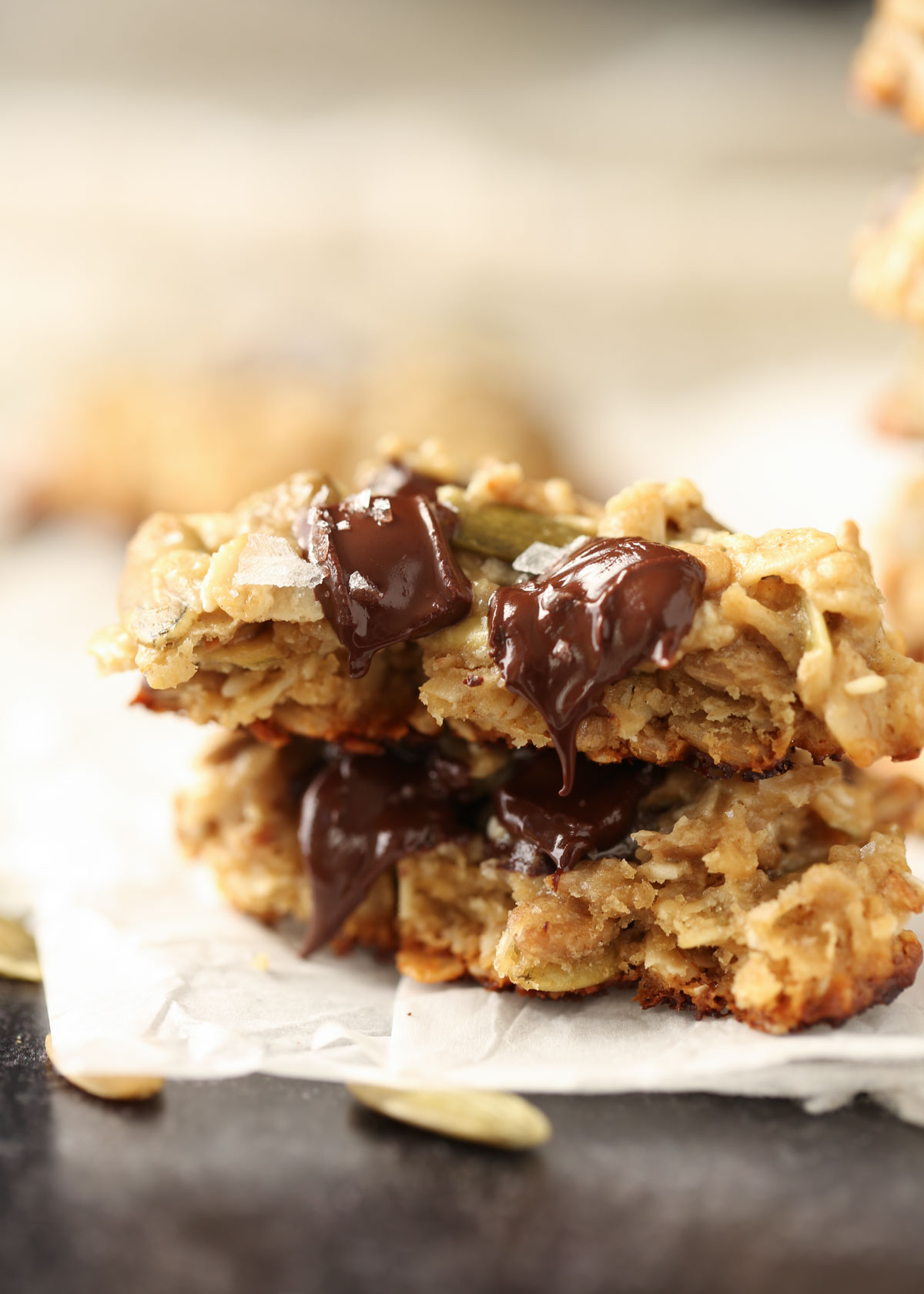 A tahini seed cookie broken in half with melty chocolate on a piece of parchment paper.
