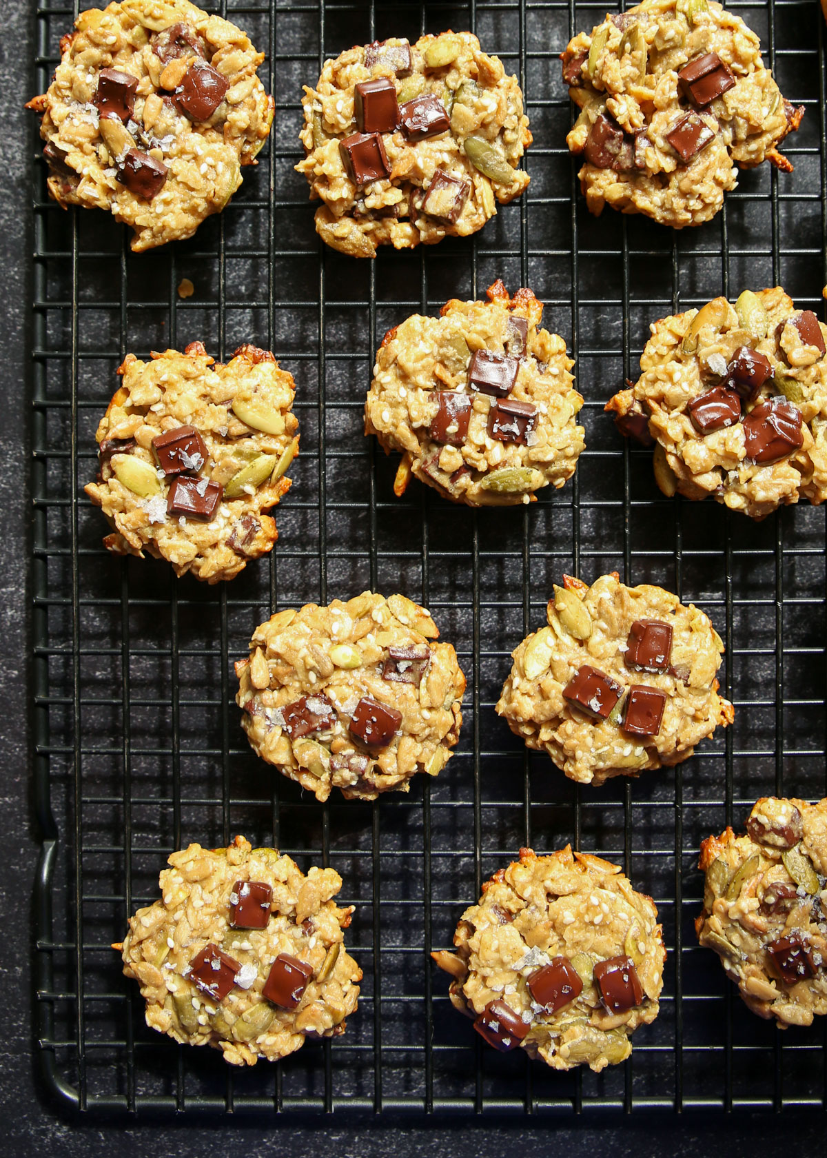 A top view of a black wire rack lined with tahini seed cookies on a black background.