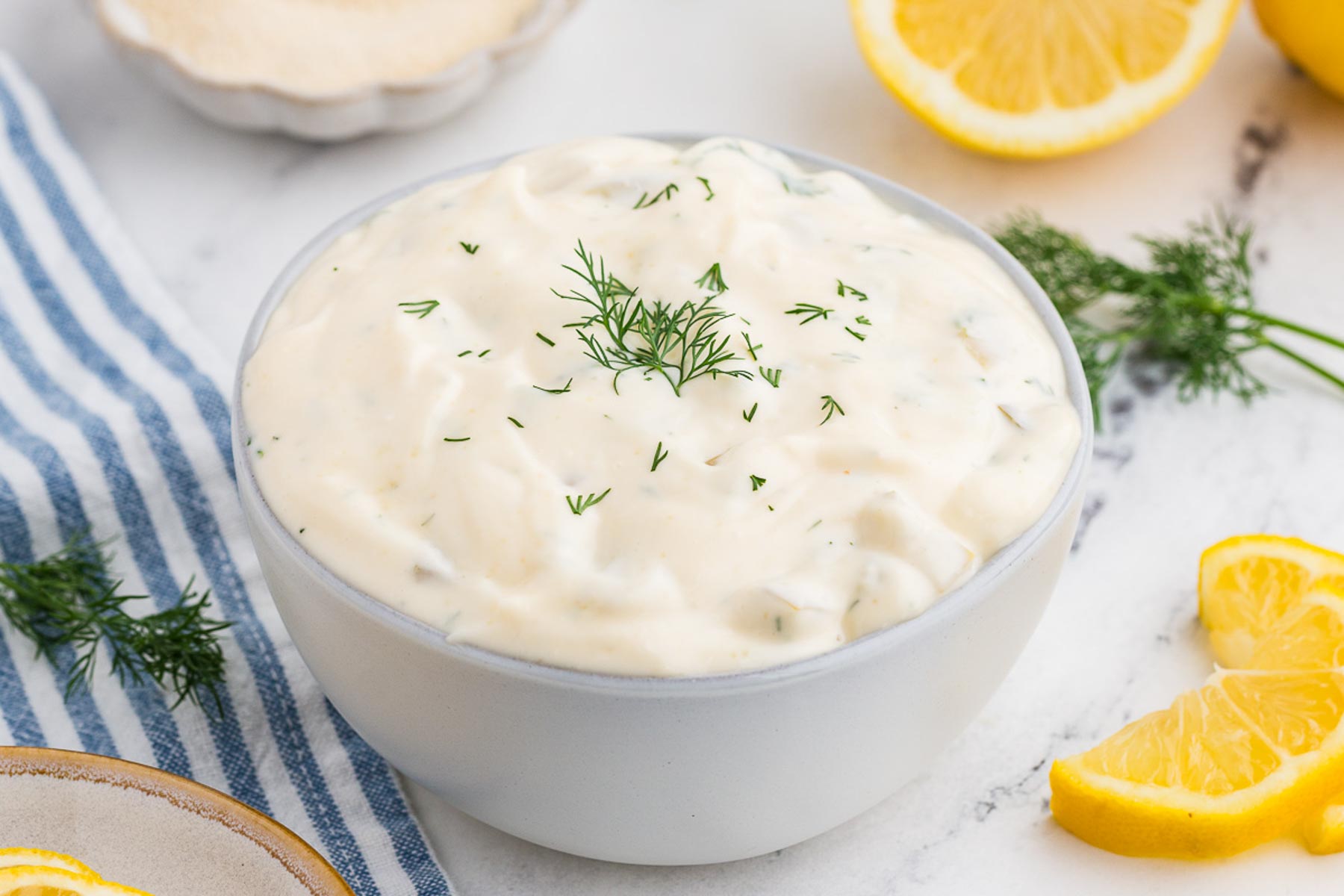 tartar sauce in a bowl with dill garnish and ingredients scattered around