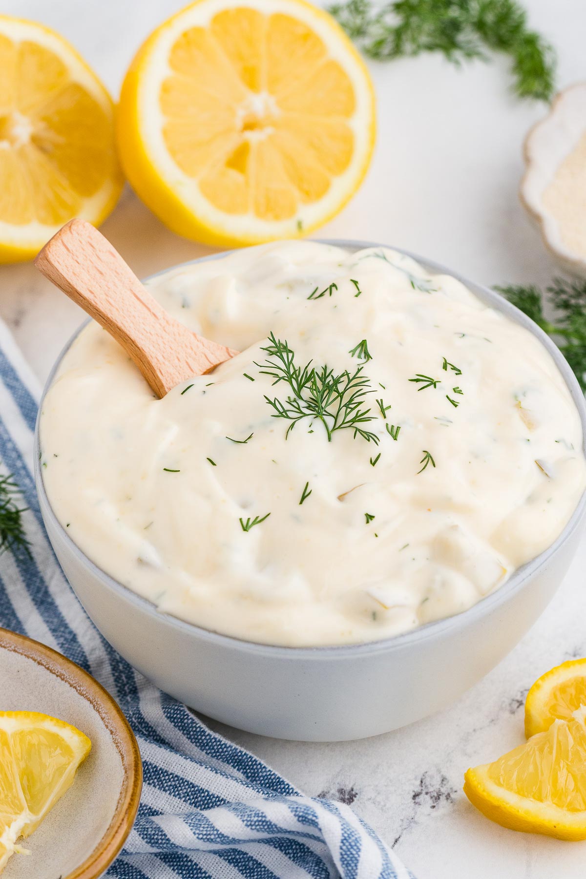 Homemade Tartar Sauce in a white bowl with dill garnish and lemons around the bowl