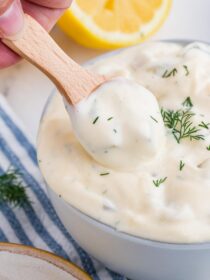 A small wooden condiment spoon scoops tartar sauce out of a bowl