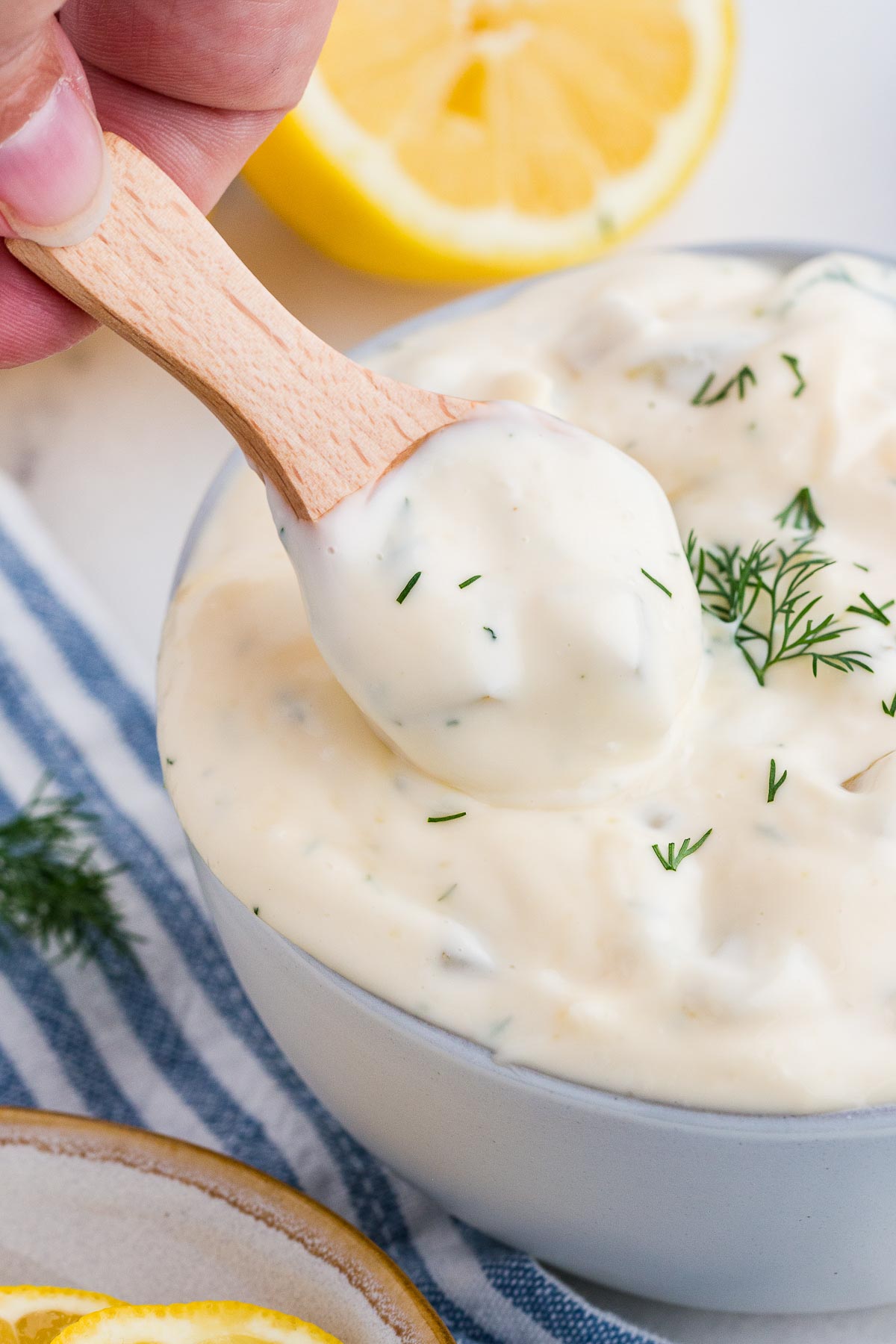 A small wooden condiment spoon scoops tartar sauce out of a bowl