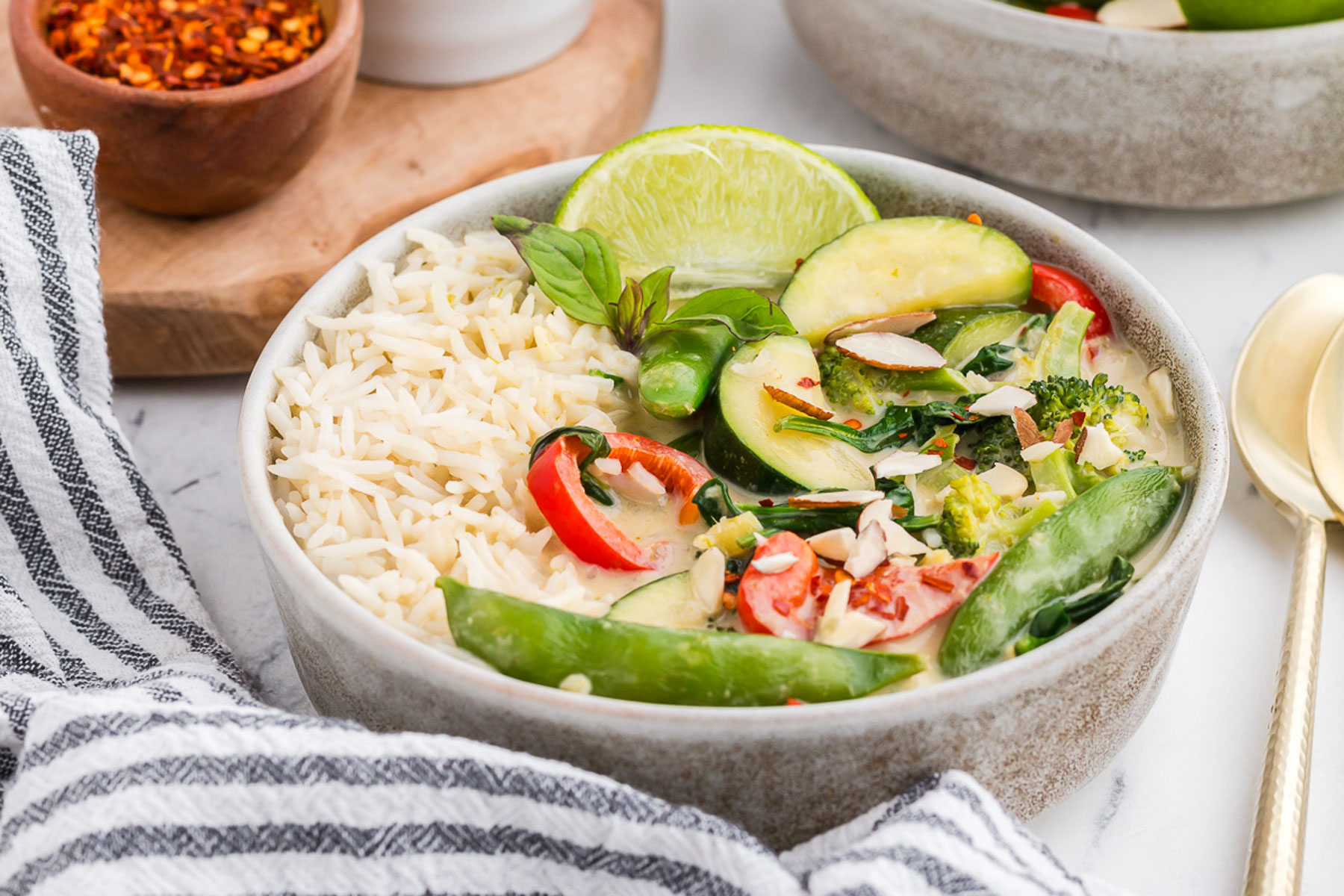A bowl of Thai green curry with a black and white striped napkin.