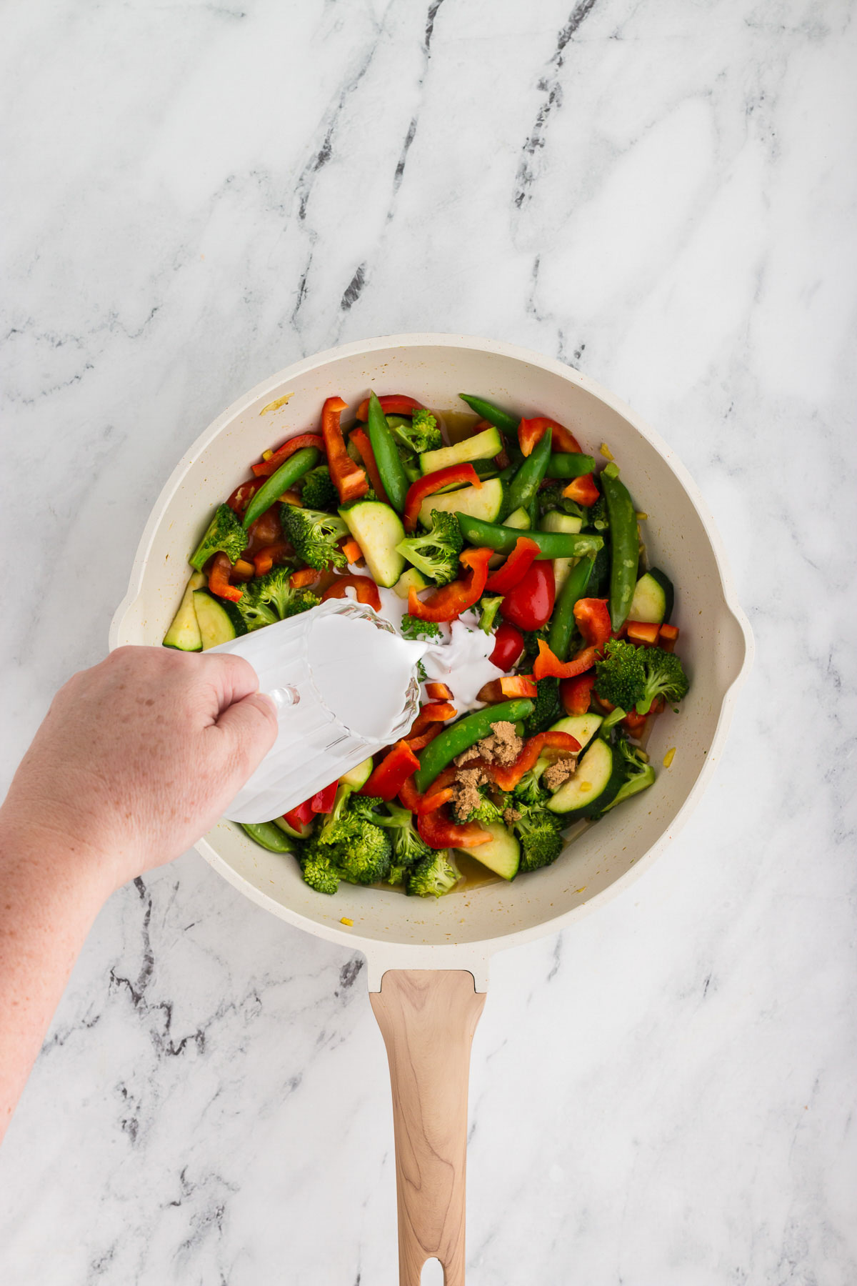 Coconut milk being added to a white skillet for Thai green curry