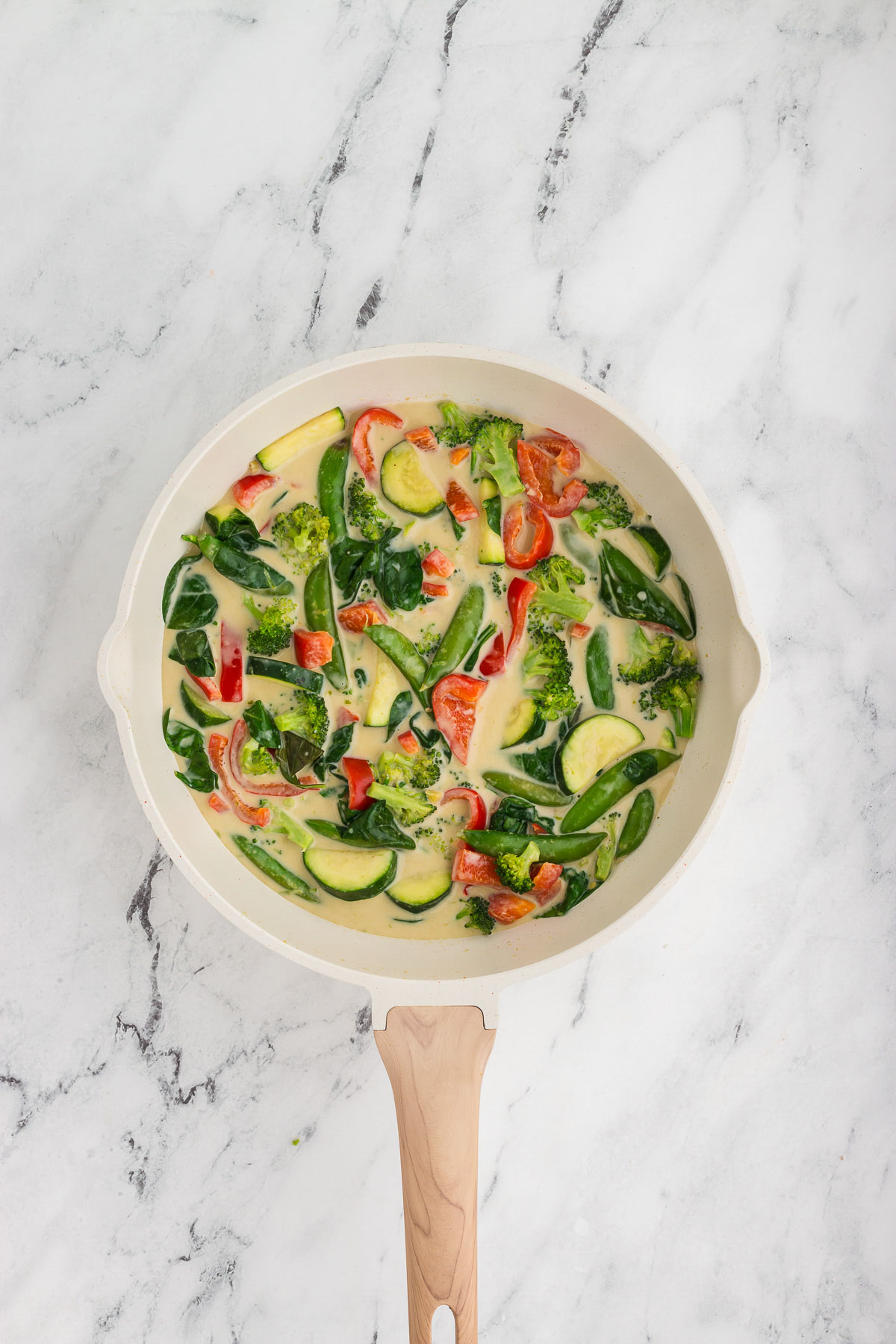 Thai green curry vegetables in a white and wood skillet