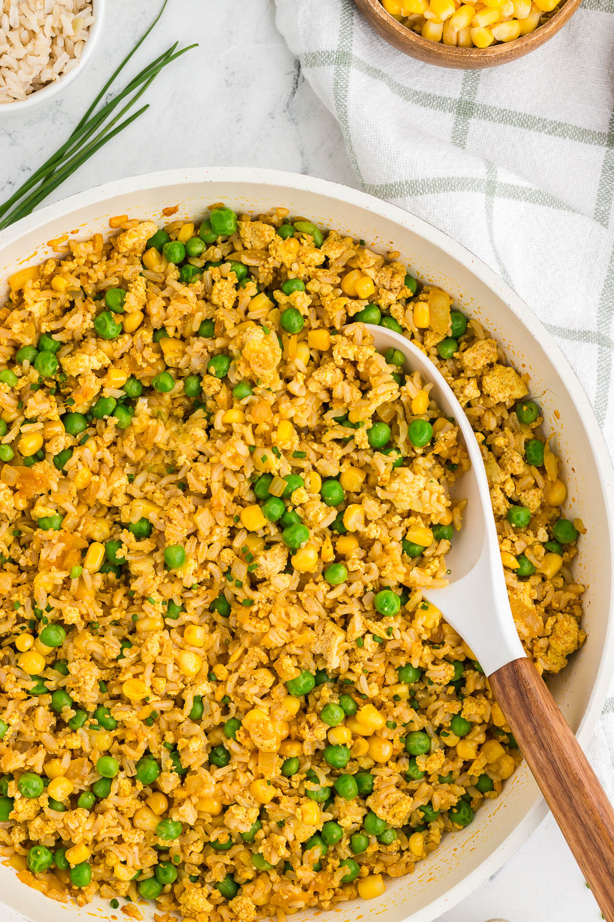 A top view of a white and wood spoon scooping tofu fried rice out of a skillet