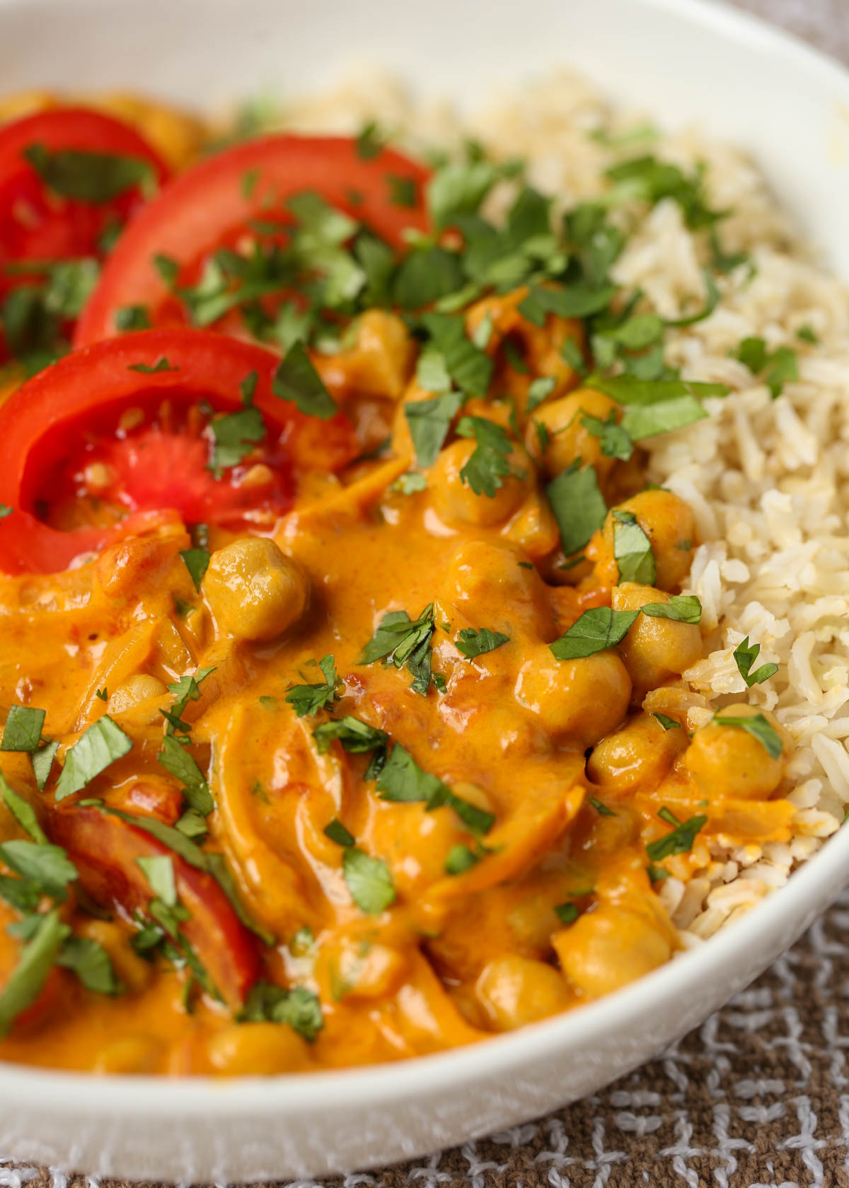 A bowl of tomato and chickpea curry with brown rice in a white bowl