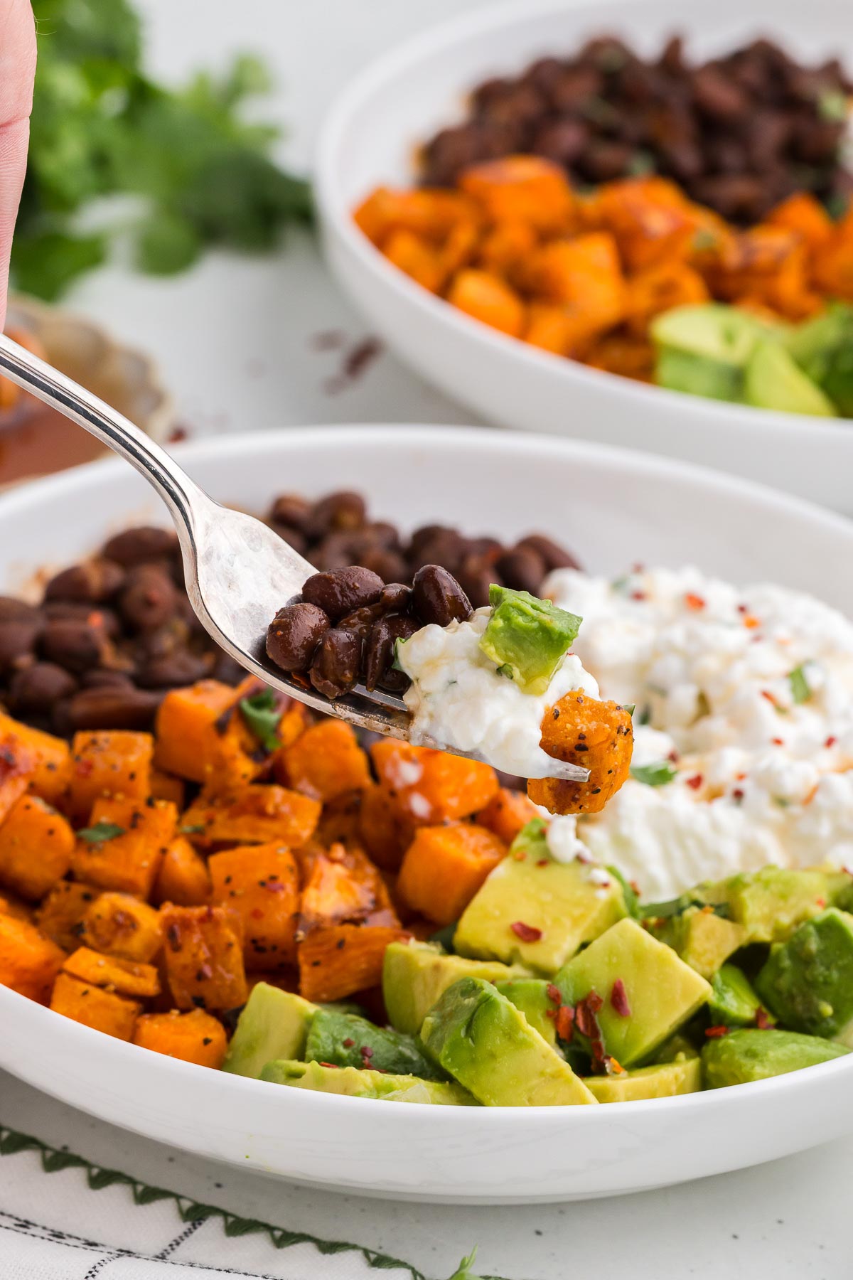 Viral Cottage Cheese Bowl in a white bowl with ingredients in the background with a fork scooping out some beans