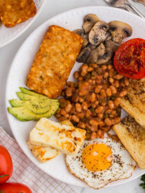 top view of vegetarian English breakfast on a white plate with tomatoes in the background