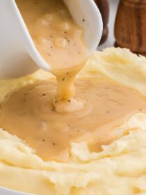 pouring vegetarian gravy over mashed potatoes in a white bowl