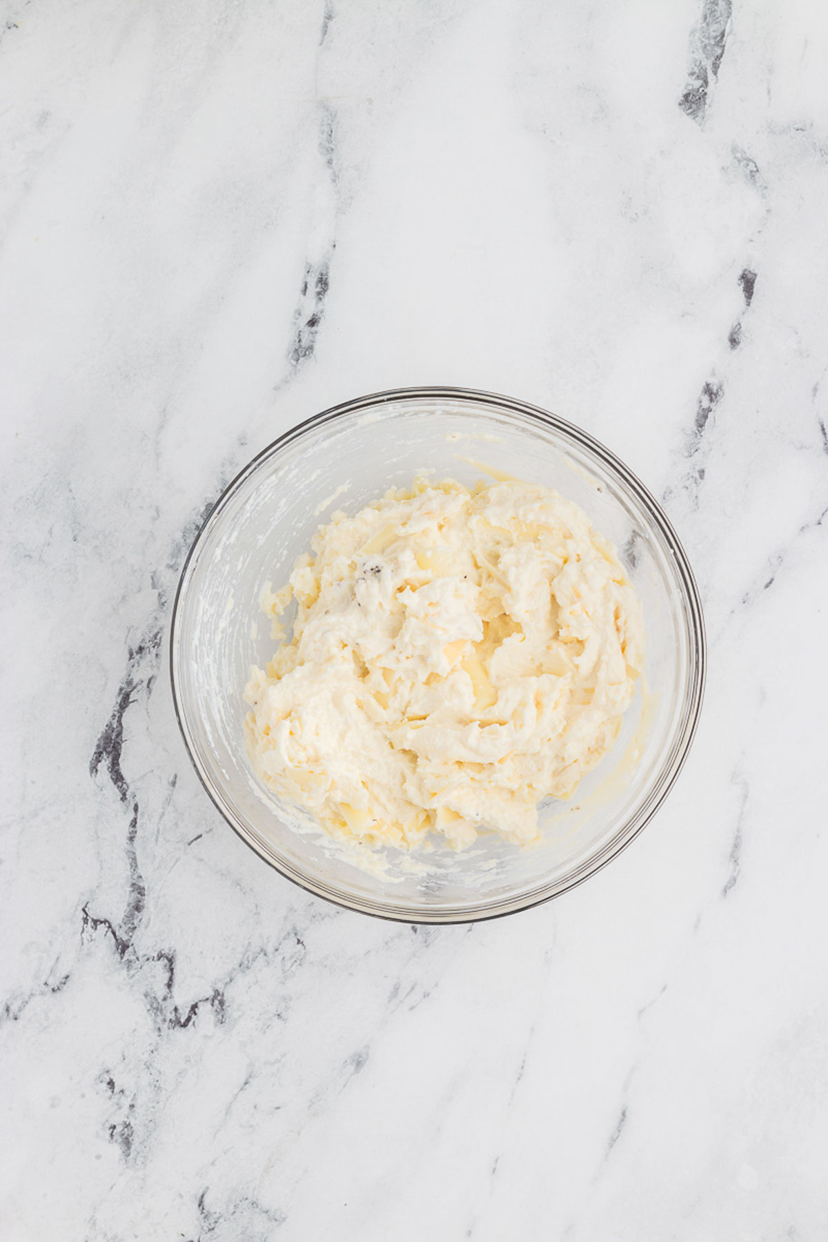 The cheesy mixture in a clear glass bowl for veggie lasagna soup.