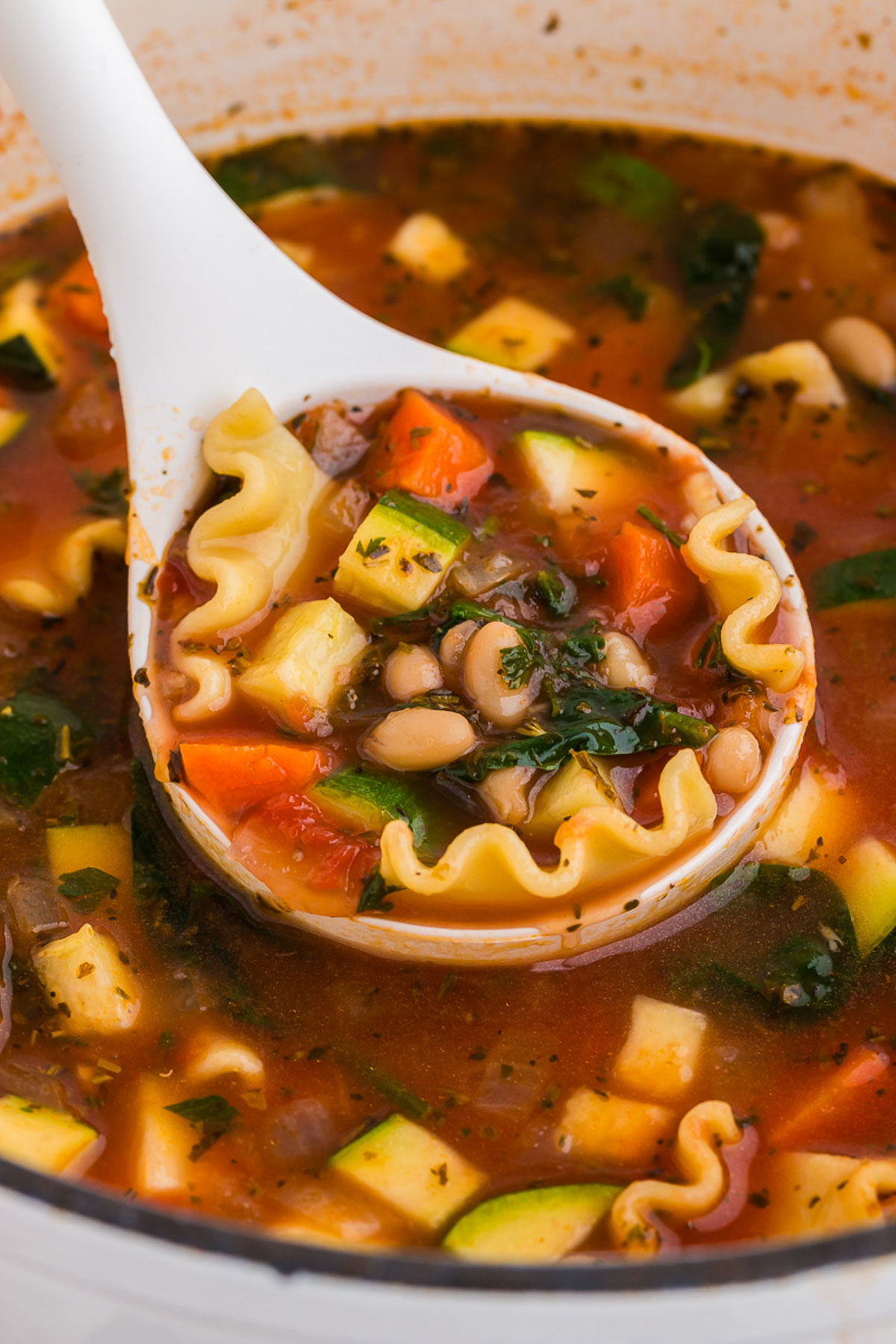 A ladleful of veggie lasagna soup is scooped out of the pot.