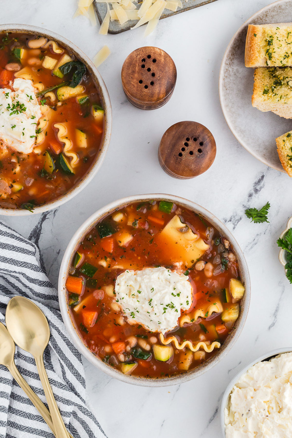 Top view of veggie lasagna soup in a rustic ceramic bowl with a gray and white striped napkin on a marble background.