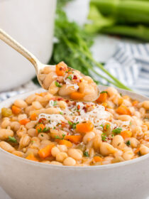 White bowl full of Vegetarian Navy Bean Soup with a gold spoon taking out a spoonful