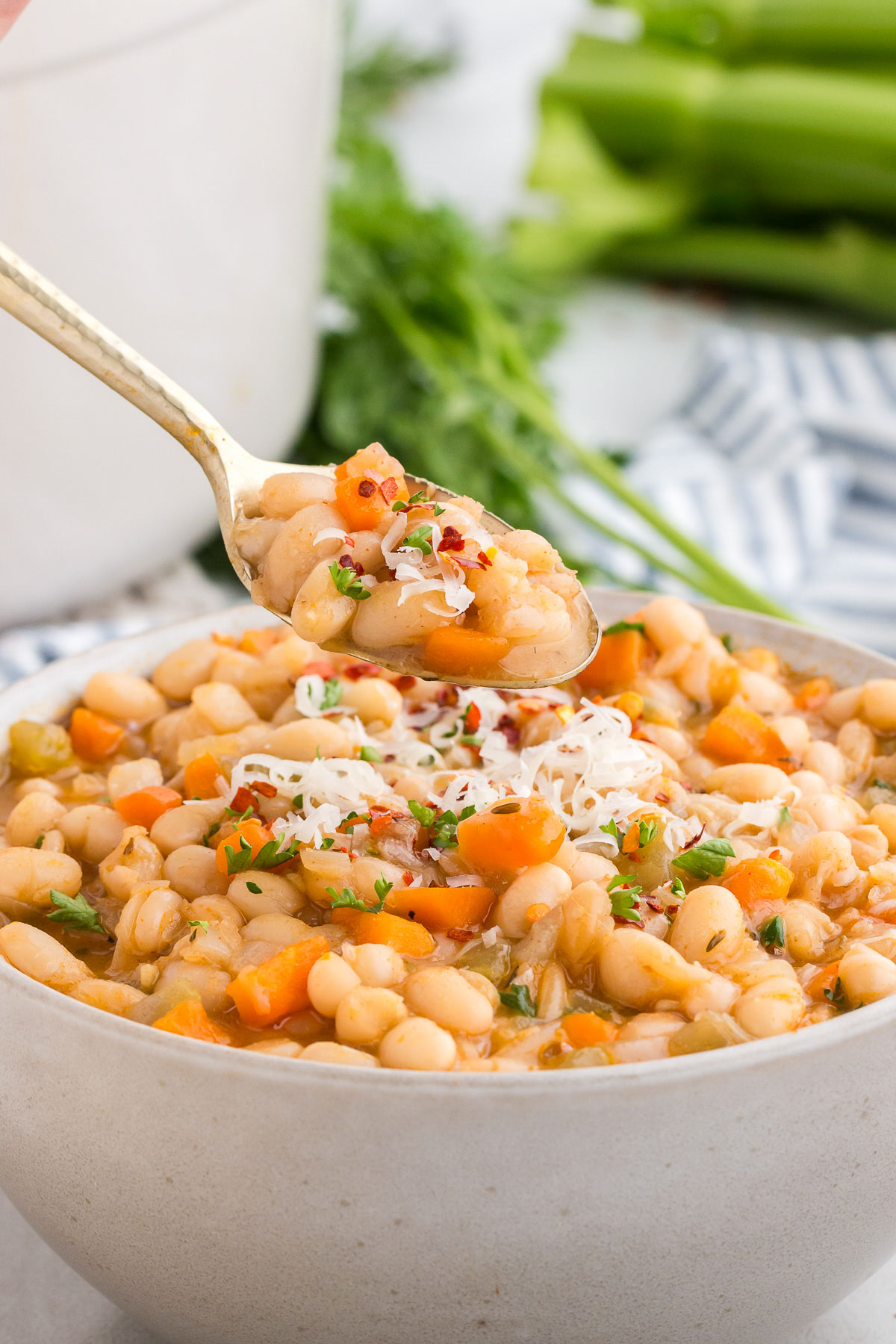 White bowl full of Vegetarian Navy Bean Soup with a gold spoon taking out a spoonful