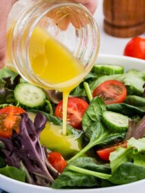 a jar of vinaigrette is poured on to a vibrant green salad