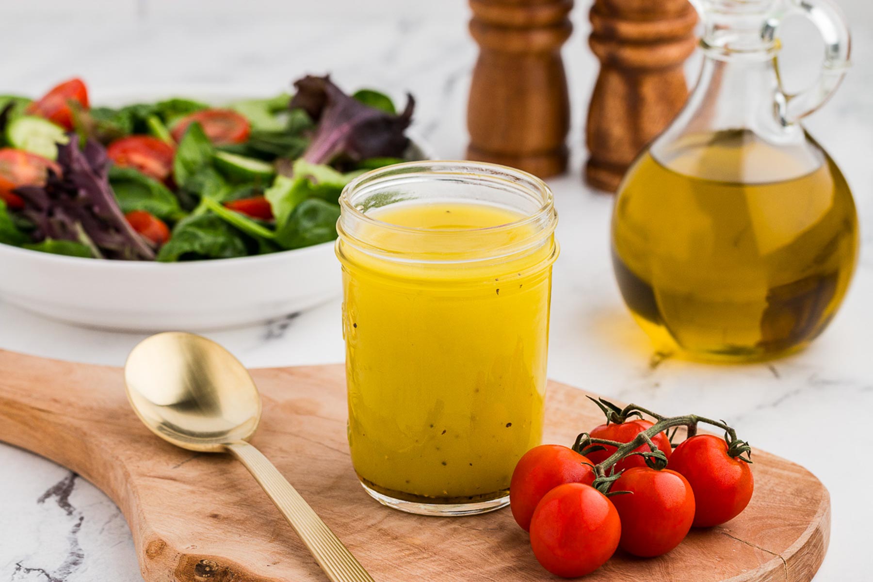 Simple salad dressing homemade vinaigrette in a mason jar with a salad and tomatoes in the background