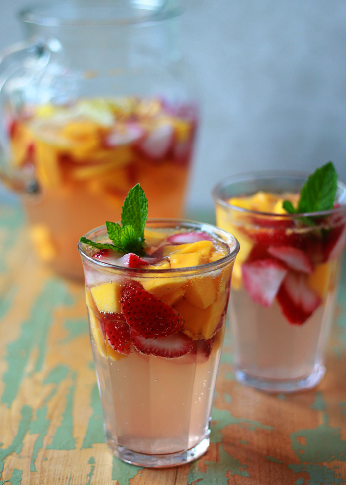 Fruity Summer Sangria with strawberries and mangos plus a mint sprig on a green background. 